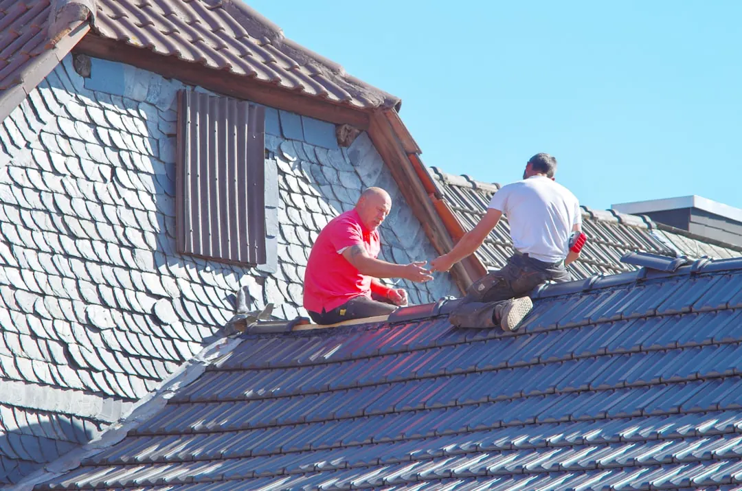 Dva pokrývači opravují střešní krytinu na rodinném domě