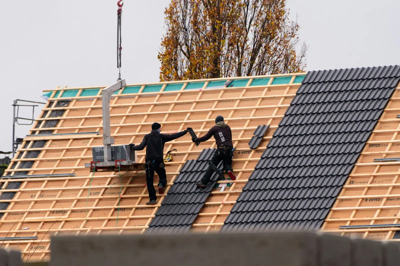 Roofers laying concrete roof tiles on a new timber roof of a family house