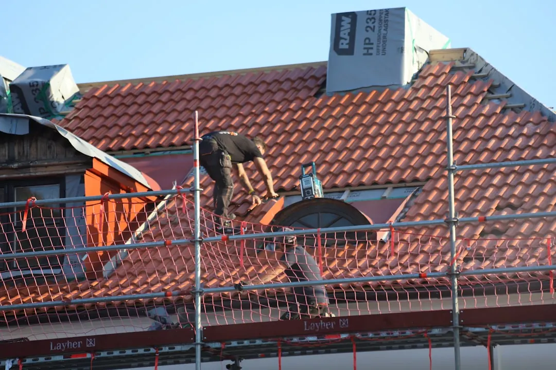 Pokrývač na lešení při práci na taškové střeše rodinného domu